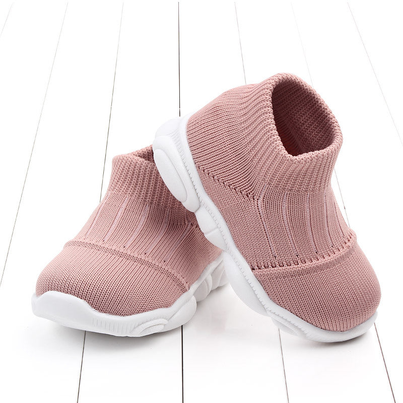 Pair of pink baby shoes with white soles on a light wooden floor.