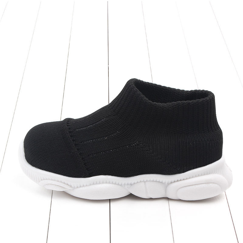 Black baby shoe with white sole on a white wooden floor
