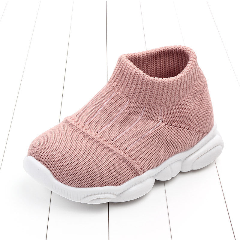 Pink baby shoe with white sole on a white wooden floor