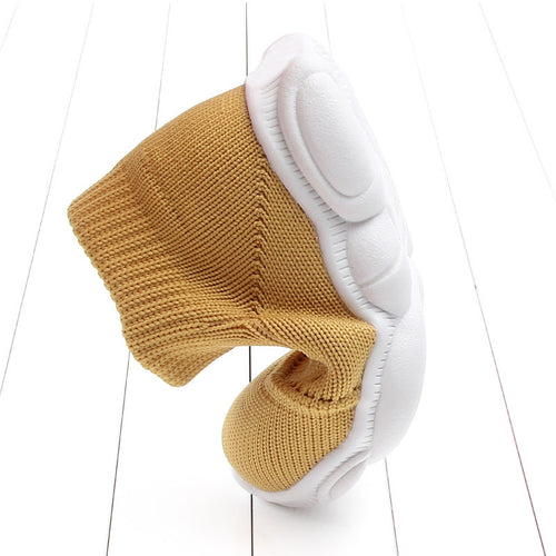 Yellow baby shoes with white soles on a white wooden floor.