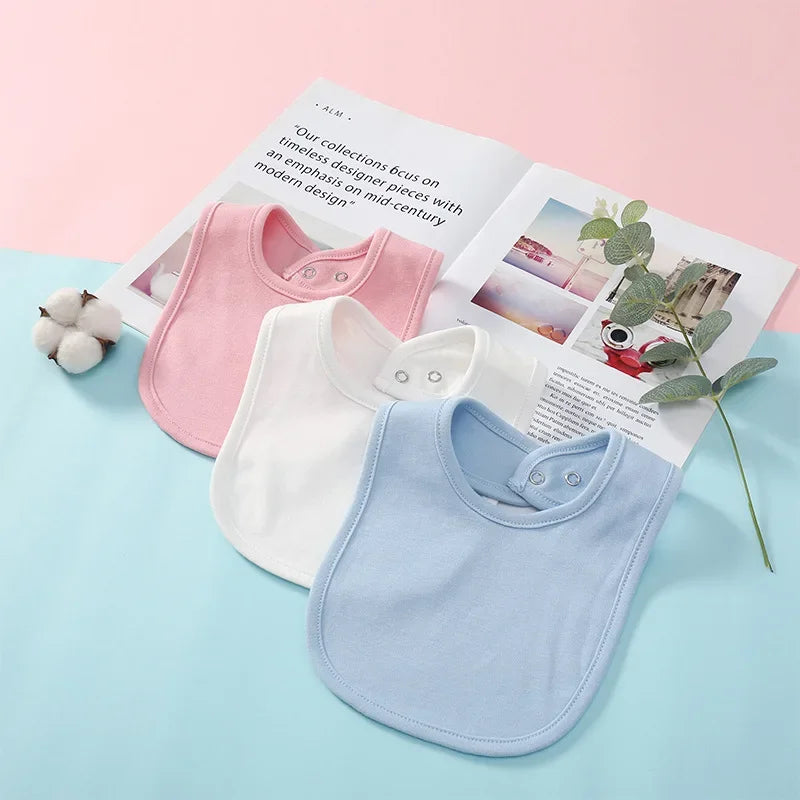 Three baby bibs in pink, white, and blue on a magazine with a light pink and blue background.