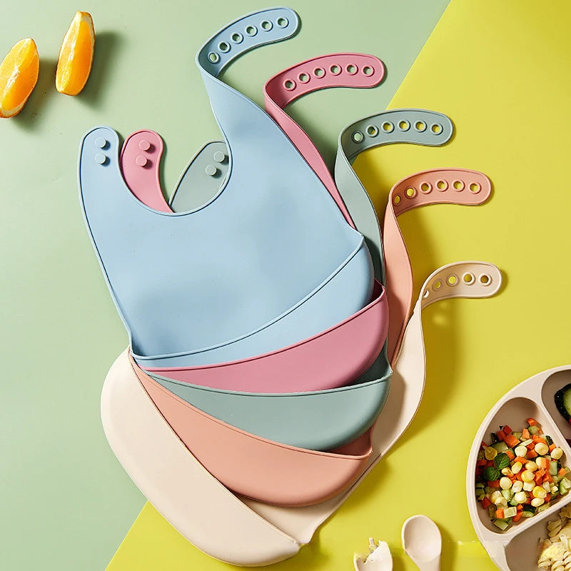Colorful baby bibs on a green and yellow background with food items.