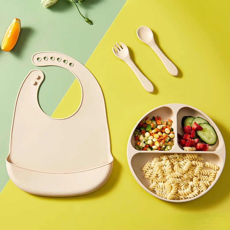 Baby bib, plate with divided sections, wooden fork, and spoon on a colorful background
