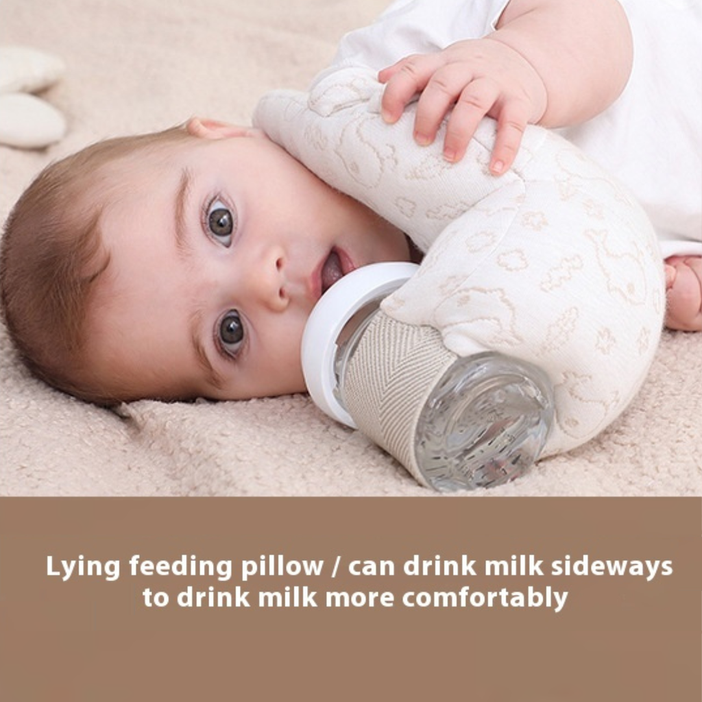 Baby lying on a beige blanket with a bottle and lying feeding pillow.