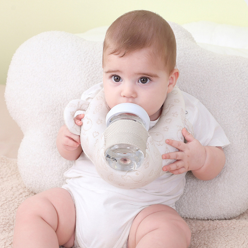 Baby holding a bottle pillow with a white pillow in the background