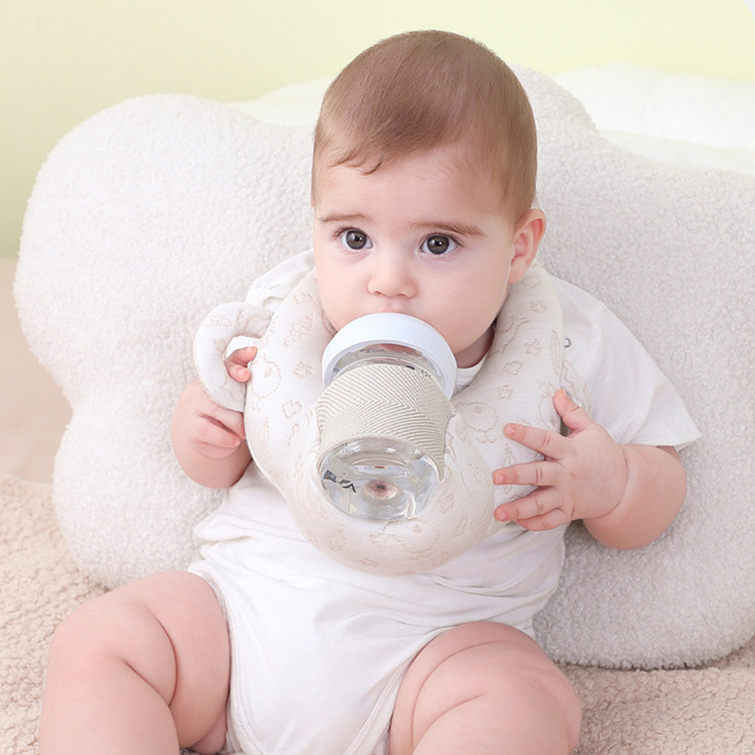 Baby holding a bottle pillow with a white pillow in the background